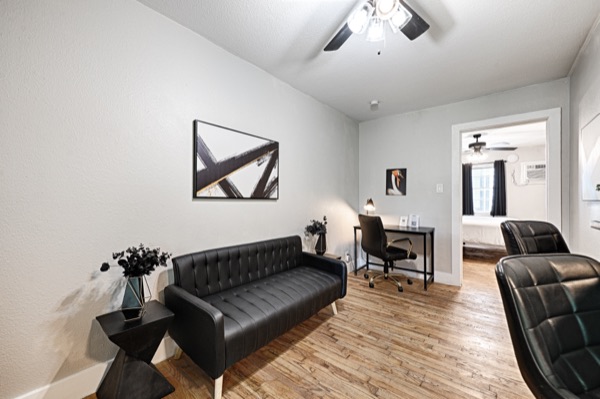 Refreshed unit living area with black leather sofa and workspace beyond
