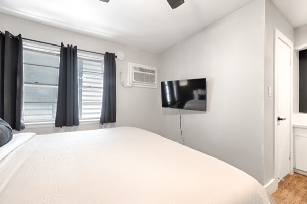Refreshed unit bedroom with king bed, black curtains and wall-mounted TV