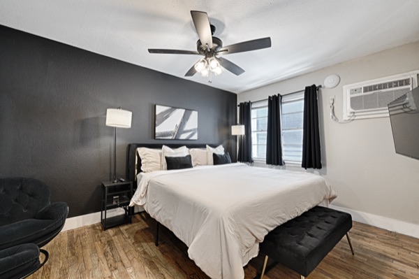 Refreshed unit bedroom, wide view with black accent wall, bench, lounge chair and AC unit